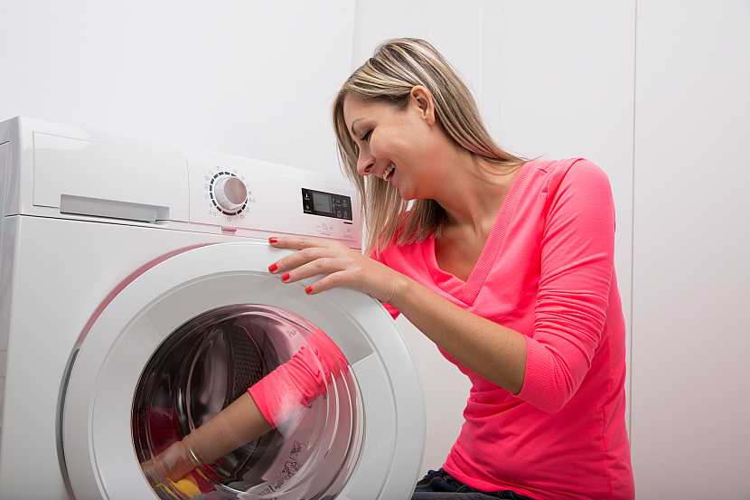 Žena sedící u pračky, která kontroluje její obsah