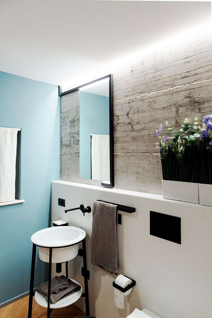 V koupelně jsou zkombinované modré stěny s betonovou stěrkou a jemnou mozaikou.