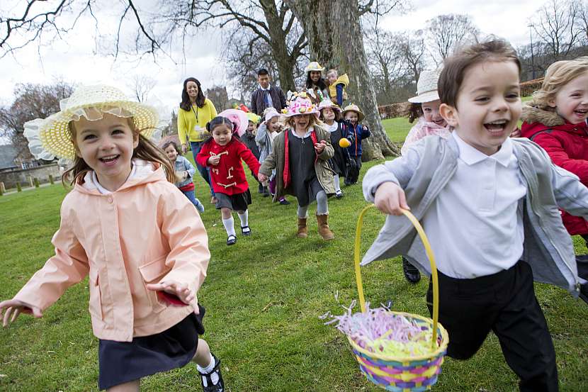 Děti pořádají hon na vajíčka, na hlavách mají velikonoční klobouky