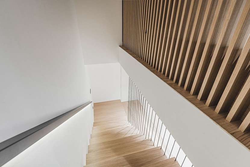 Zábradlí tvoří ve spodní části kovové černé tyče a v patře chrání před pádem ze schodů dřevěné žebrování.