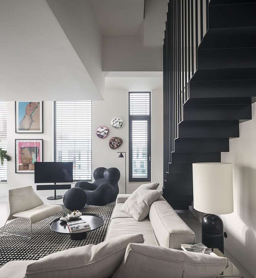 Dominantou obývacího pokoje je atypicky řešené schodiště ze subtilního černého lakovaného plechu, pod kterým se rozkládá sněhobílá pohovka doplněná ikonickým křeslem UP 50 od B&amp;B Italia.
