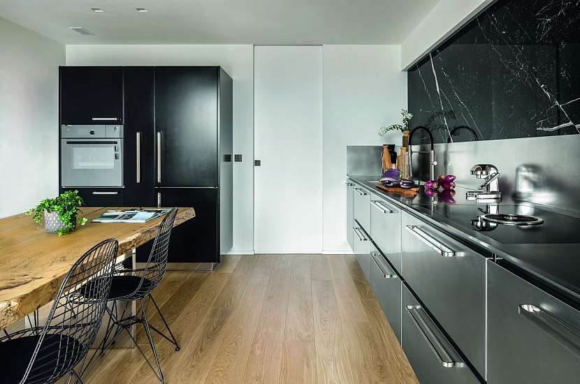 Luxusní ocelová kuchyně skvěle zapadá do moderního interiéru a horní skříňky v dekoru černého mramoru, dřevěná podlaha i originální stůl z masivního dřeva zjemňují kovové plochy linky.
