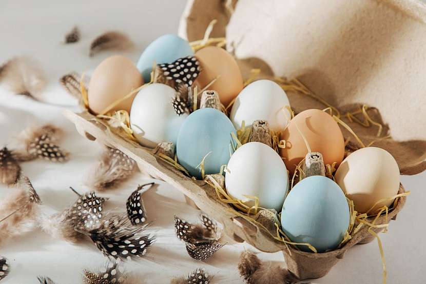 Geniálně jednoduché – barevná vajíčka naskládejte na papírové plato, které před tím vyložíte trochou sena a dozdobte ledabyle pírky.