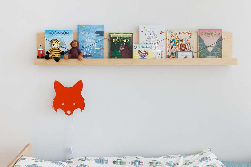 Nad postelí se nachází police na knihy, které jsou uchyceny gumičkou vytvářející “klikyhák”. .