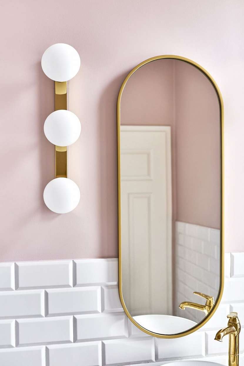 Stěnu v odstínu pudrově růžové ozdobila zrcadlem ve zlatém rámu a efektním svítidlem s oblými stínidly.
