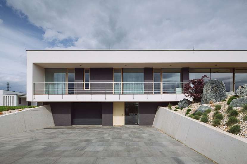 Předprostor domu, který je zařezán do terénu, je jedním z výrazných prvků návrhu. Jeho nálevkovitý tvar uživatele vítá a vtahuje dovnitř.
