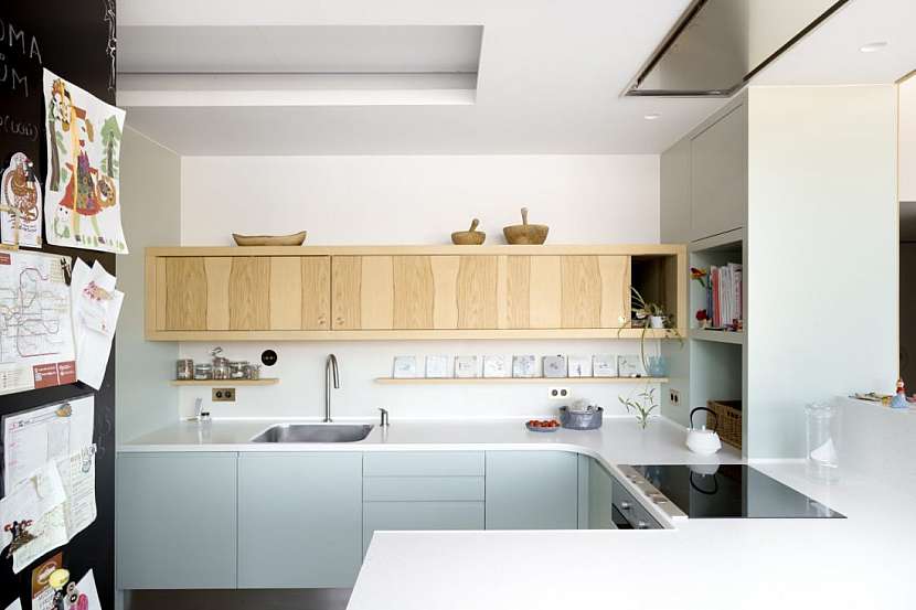Kuchyňská linka má dolní skříňky v moderní mentolové barvě, zatímco nízké horní skříňky jsou vyrobeny ze dřeva.