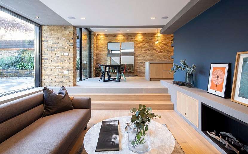 Obývací pokoj s krbem je uložen níže pod úroveň jídelny, což pomáhá vymezit jednotlivé funkční zóny společného prostoru. .