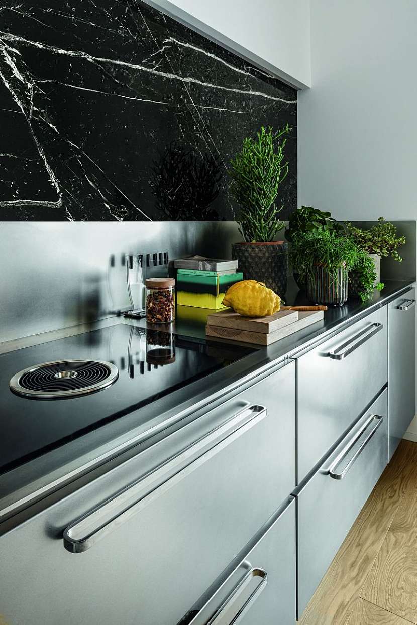 Luxusní ocelová kuchyně skvěle zapadá do moderního interiéru a horní skříňky v dekoru černého mramoru, dřevěná podlaha i originální stůl z masivního dřeva zjemňují kovové plochy linky.
