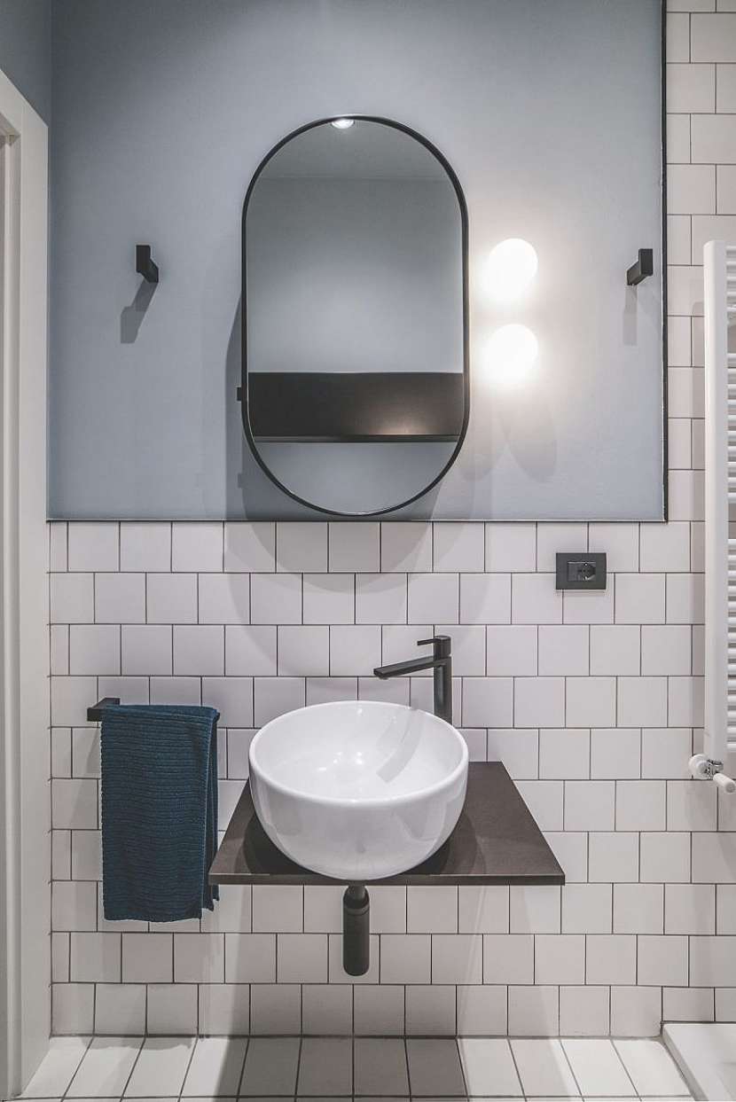 Malá koupelna se vyznačuje bílými čtvercovými dlaždicemi kontrastujícími s pastelově modrými stěnami.