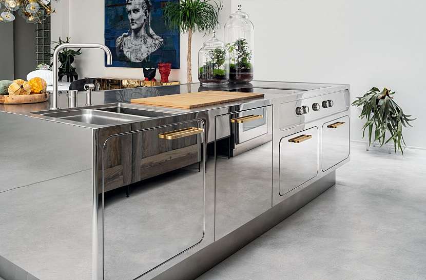 Kuchyň z nerezové oceli odráží světlo díky zrcadlovému provedení, rafinovanost jí dodávají velká ergonomická držadla v mosazné úpravě.