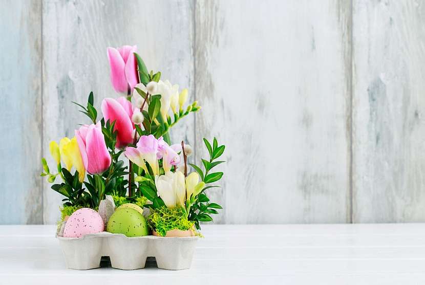 Velikonoční květinová dekorace s barevnými vajíčky, tulipány, fréziemi a buxusem.