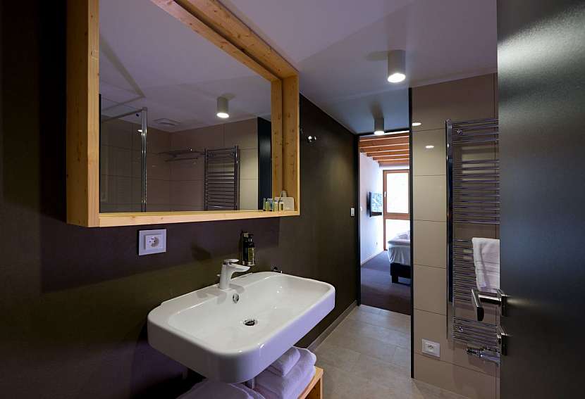 Koupelna v tmavých tónech a přírodním dřevu.