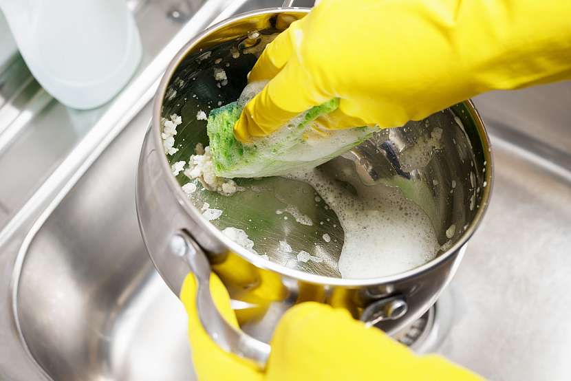 Umývání hrnce pod vodovodním kohoutkem houbičkou a v rukavicích