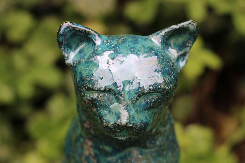 Sytě modrá sedící kočka s glazurou, která zanechává na šamotové hlíně proměnlivou strukturu různých odstínů modré.