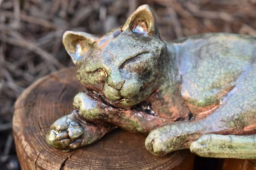 Na obrázku je ručně modelovaná socha kočky glazovaná zelenou a měděnou glazurou a pálená technikou raku. (Zdroj: Karolína Bathory)