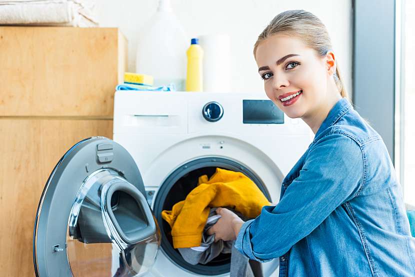 Žena u pračky s prádlem v ruce