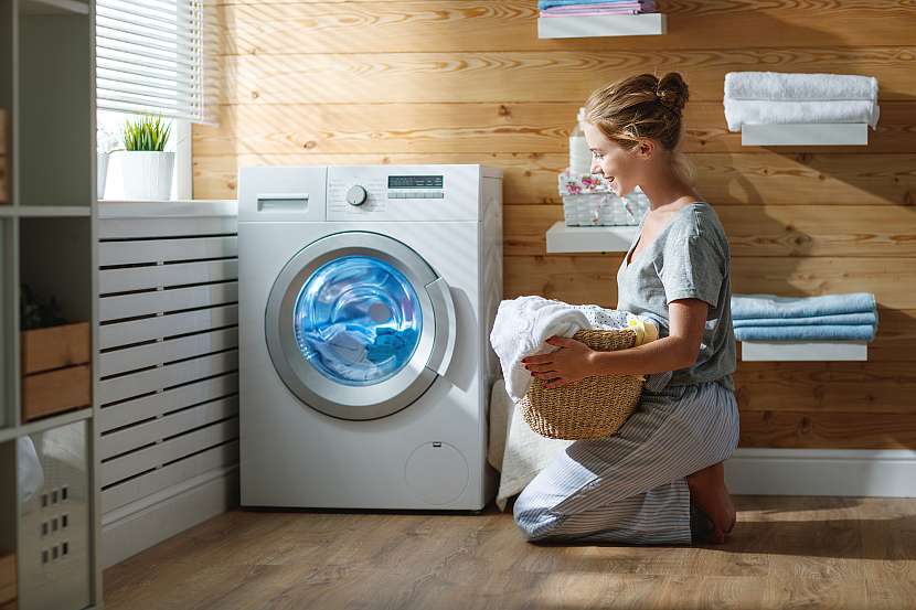 Žena klečící u pračky s košem prádla