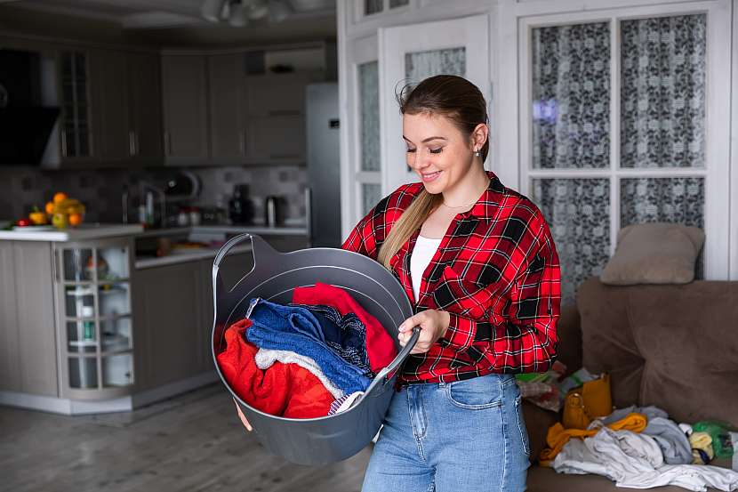 Žena drží plastový koš se špinavým prádlem